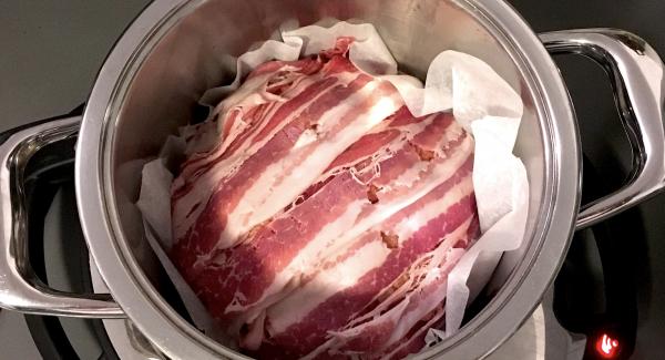 Den Braten mit Hilfe des Backpapiers in den heißen Topf geben. Ein Glas Wasser mit dem  halben Brühwürfel dazu geben