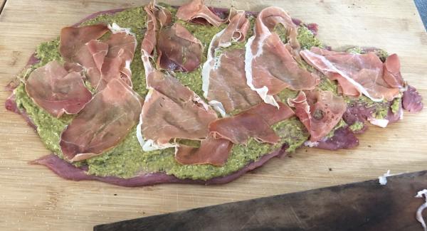 Sobald das Schweinefilet schön flach ist, das Fleisch mit 2 EL Pesto bestreichen. Danach mit ca. 80g Serrano Schinken belegen.