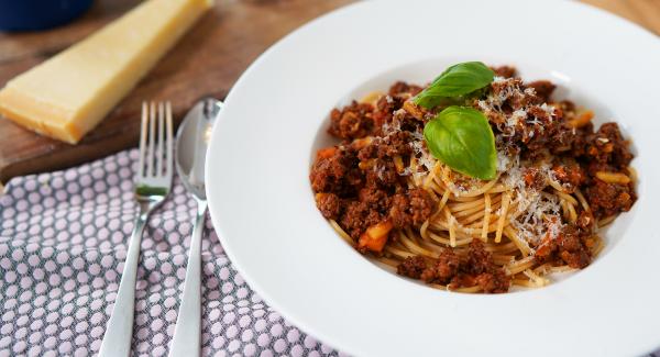 Die Spaghetti Bolognese mit gehobelten Parmesan verfeinern.