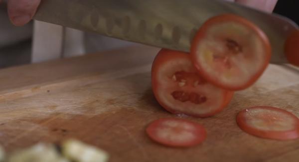 Eine Tomate in dünne Scheiben schneiden.