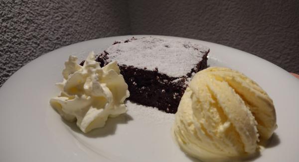 Ein Stück Schweizer Schoggikuchen mit einer Kugel Vanille Glace und einem Tupfer Rahm servieren.